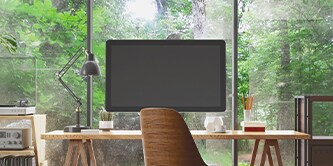 Monitor på et skrivebord, med en skov synlig i baggrunden
