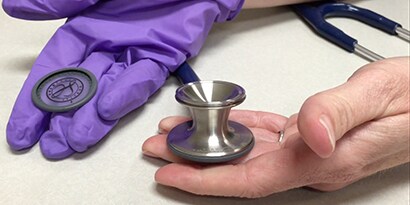Hænder, der holder et 3M ™ Littmann® Classic III ™ Stetoskopbryststykke og aftagelig enhed.
