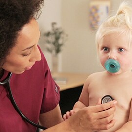 Pædiatrisk sygeplejerske, som lytter til brystet på et lille barn med et 3M Littmann Classic III stetoskop. 