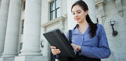 Kvinde med en tablet foran en offentlig bygning

