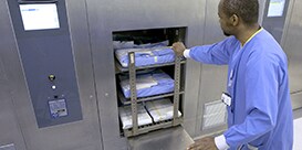 Person på central sterilisering skubber instrumentvognen ind i autoclaven
