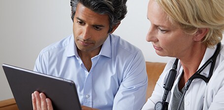 Læge, der auskulterer og viser en mand appen på en tablet
