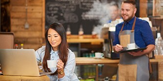 Kvinde, der sidder på en café og arbejder på sin bærbare computer
